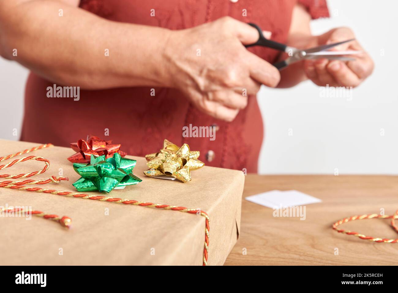 Unkenntlich reife Frau, die mit einer Schere Stücke aus weißem Karton schneidet und handgefertigte Karten für ihre Weihnachtsgeschenke macht. Selective Focus Desi Stockfoto