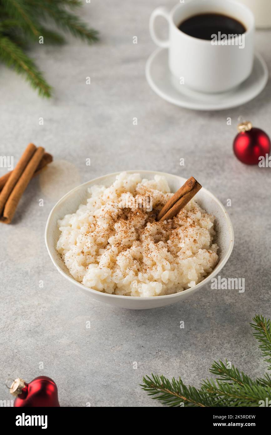 Skandinavischer Reisbrei mit Zimt in einer Schüssel, umgeben von Weihnachtskugeln. Frühstück am Heiligabend. Stockfoto