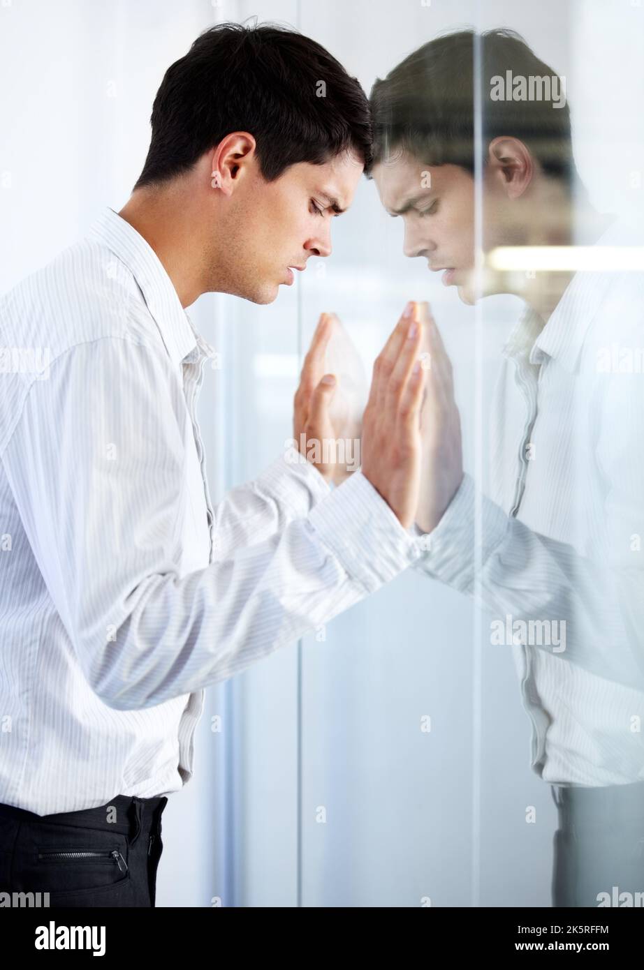 Ich schlug mit dem Kopf gegen eine Glastür. Ein junger Geschäftsmann, der seinen Kopf gegen eine Glastür drückt und Negativität ausdrückt. Stockfoto