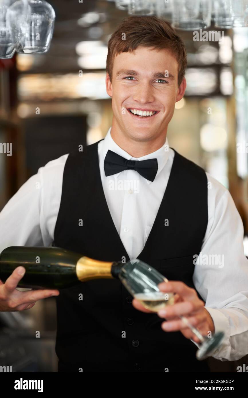 Besondere Anlässe feiern. Fröhlicher junger Waiterbarmann, der lächelt, während er ein Glas Champagner ausgießt. Stockfoto