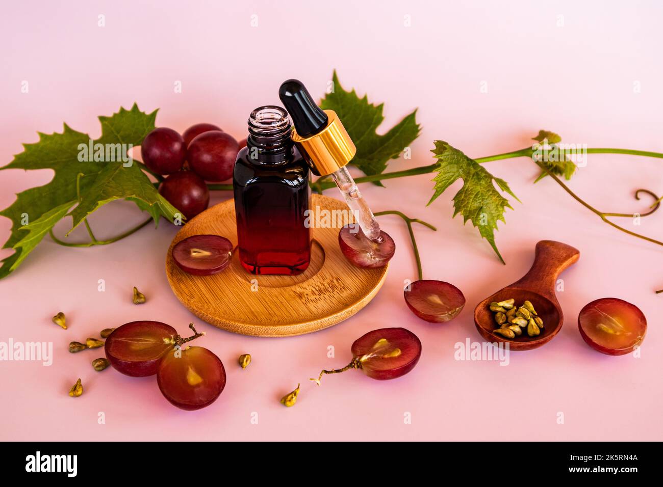 Molke- oder Traubenkernöl in einer farbigen Flasche auf einem Holzteller mit einer mit Kosmetik gefüllten Pipette. Natürliche Hautpflege Stockfoto