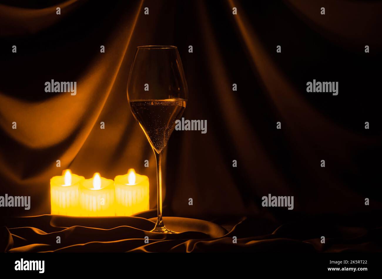 Ein Glas Weißwein mit verschwommenen Fokuskerzen auf dunklem Stoffhintergrund. Halloween Dinner Party Konzept. Stockfoto