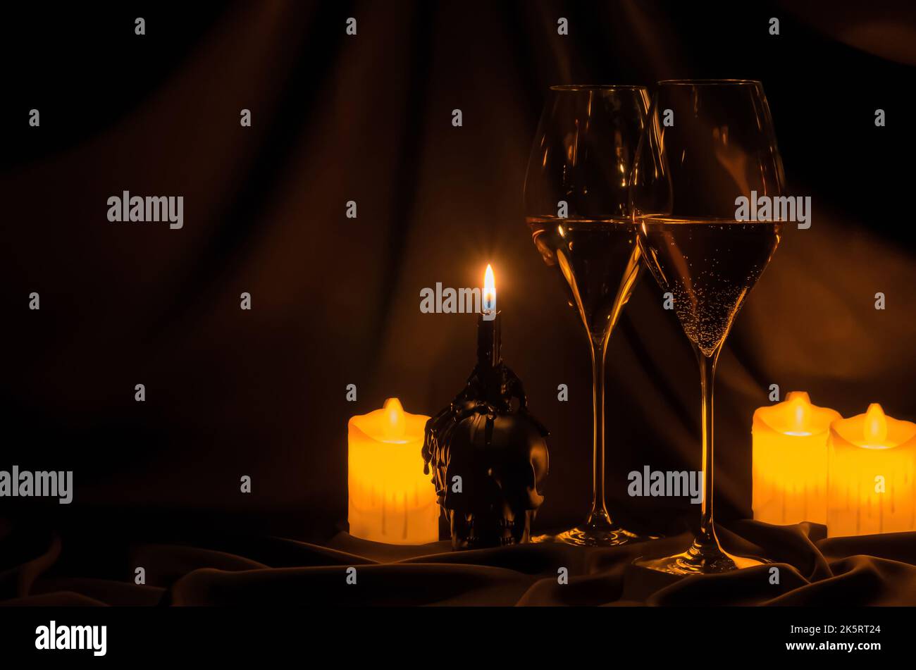 Gläser Weißwein mit verschwommenem Fokusschädel und Kerze auf dunklem Stoffhintergrund. Halloween Dinner Party Konzept. Stockfoto