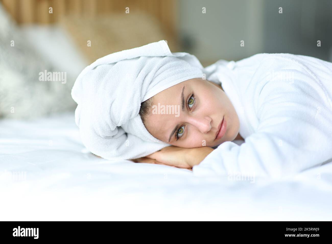 Schönheitsfrau mit grünen Augen schaut auf die Kamera, die auf dem Bett liegt Stockfoto