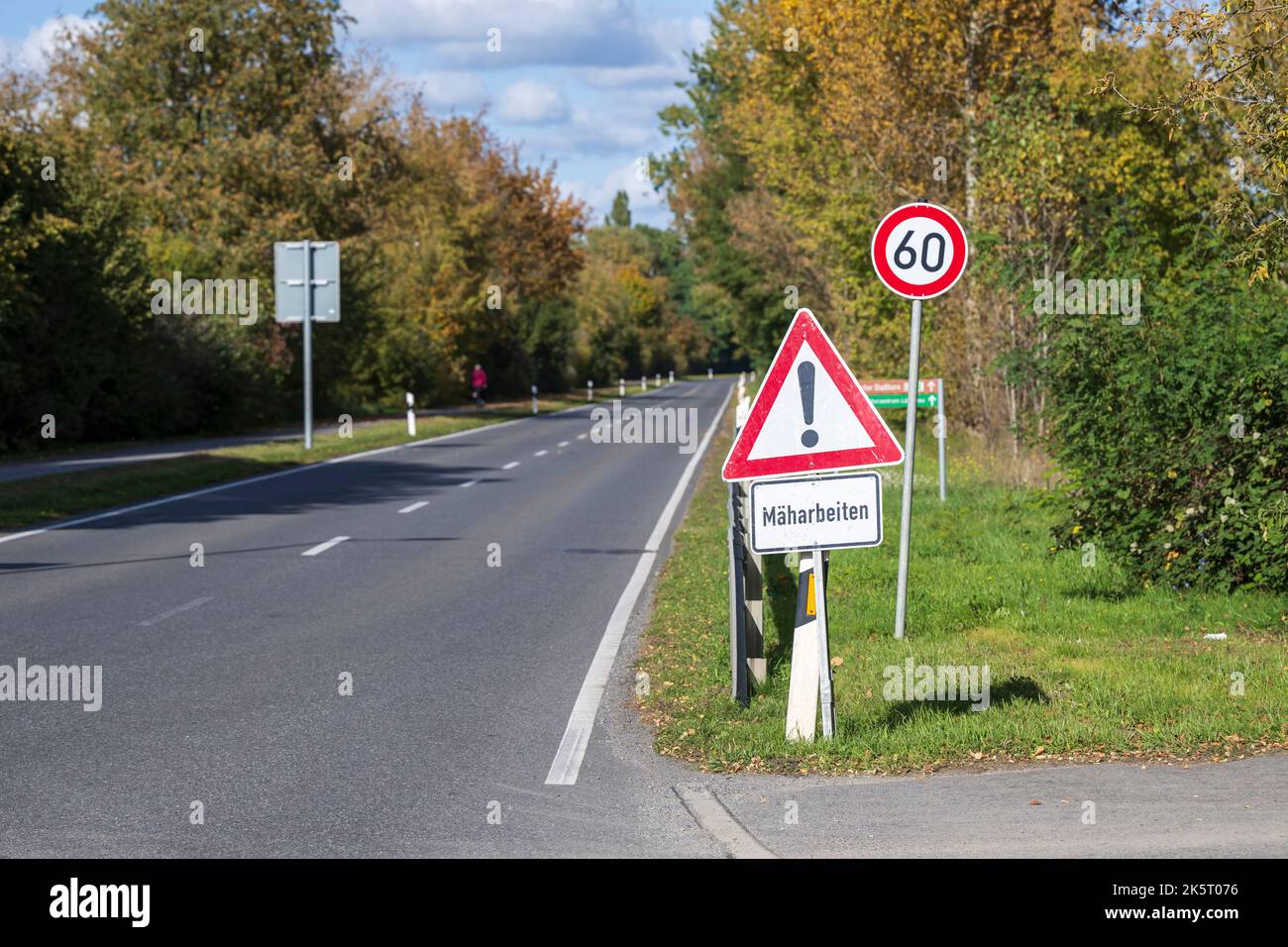 Ein Warnschild mit dem zusätzlichen Schild in deutscher Sprache , Mäharbeiten , am Straßenrand Stockfoto