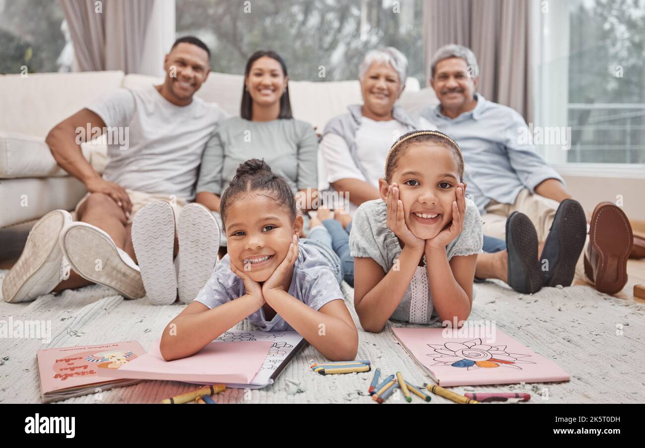 Zwei niedliche Geschwisterschwestern mit gemischter Rasse, die im Wohnzimmer zeichnen und färben, mit ihren Eltern und Großeltern im Hintergrund. Unbeschwerte Kinder Stockfoto