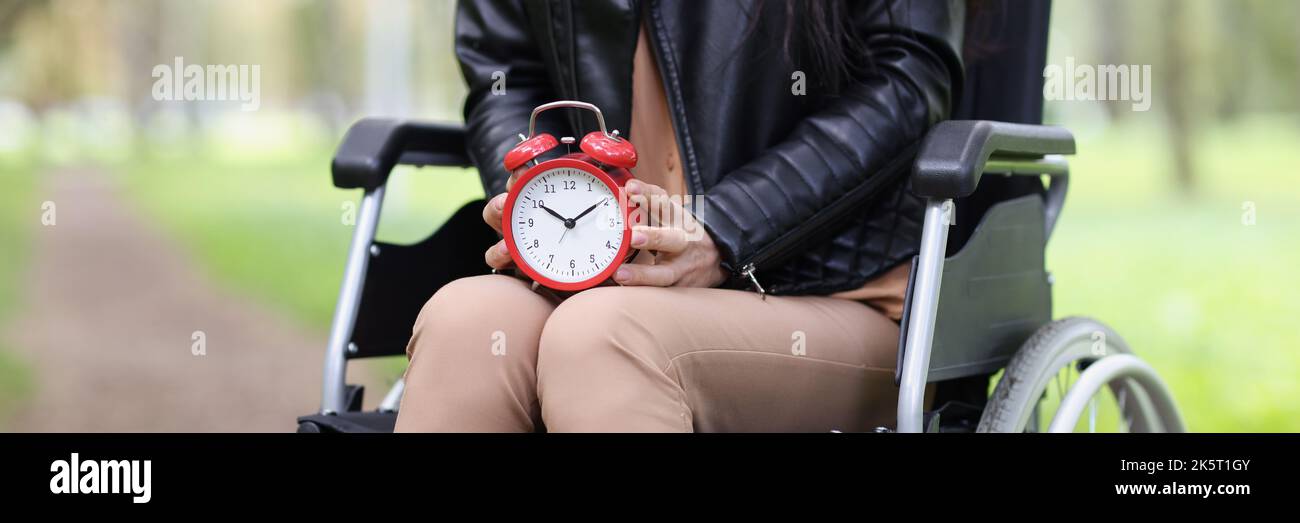 Frau im Rollstuhl hält Wecker im Park Stockfoto