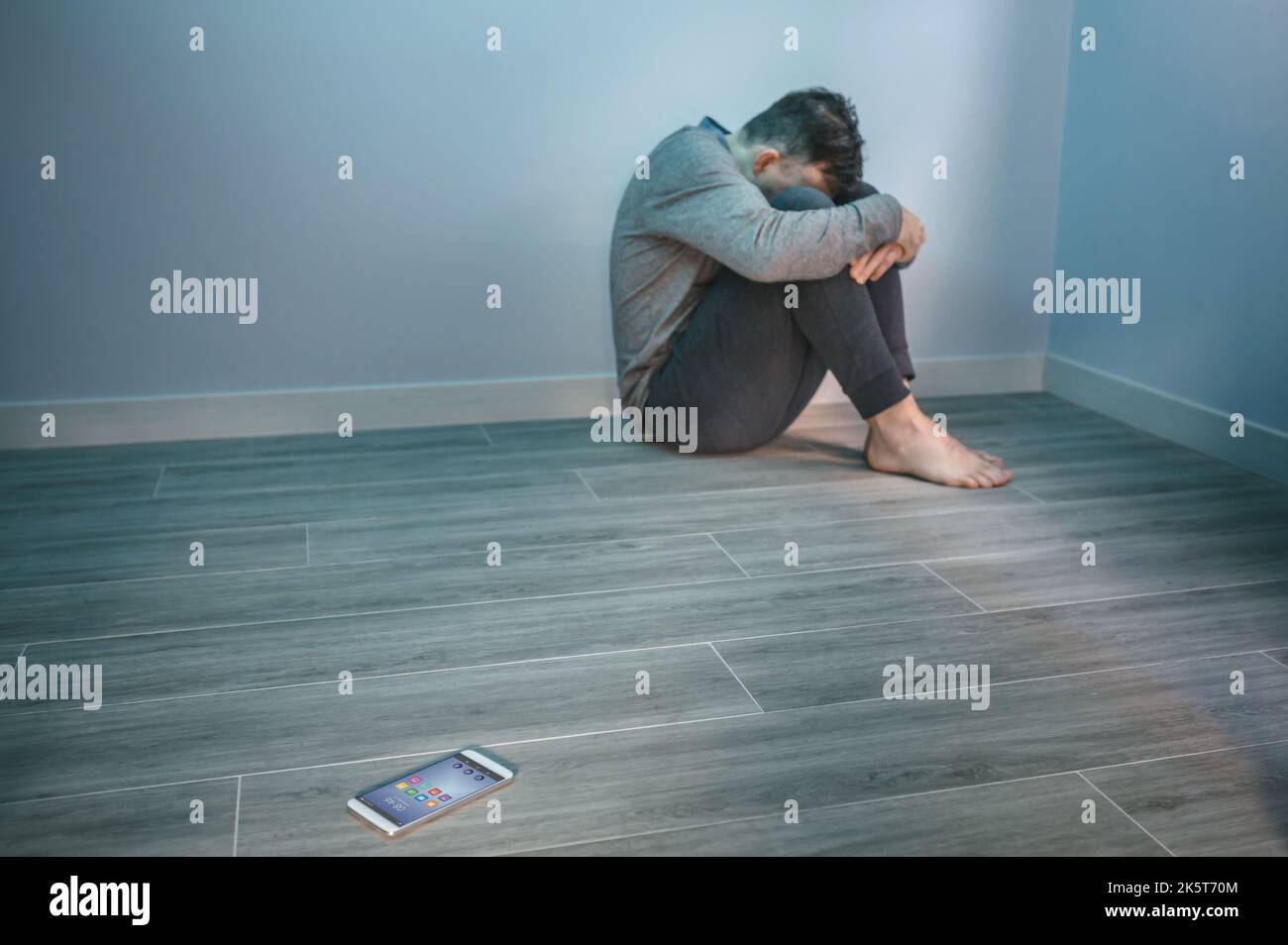 Mann mit Problemen, der auf dem Boden saß und ein Handy auf dem Boden hatte Stockfoto