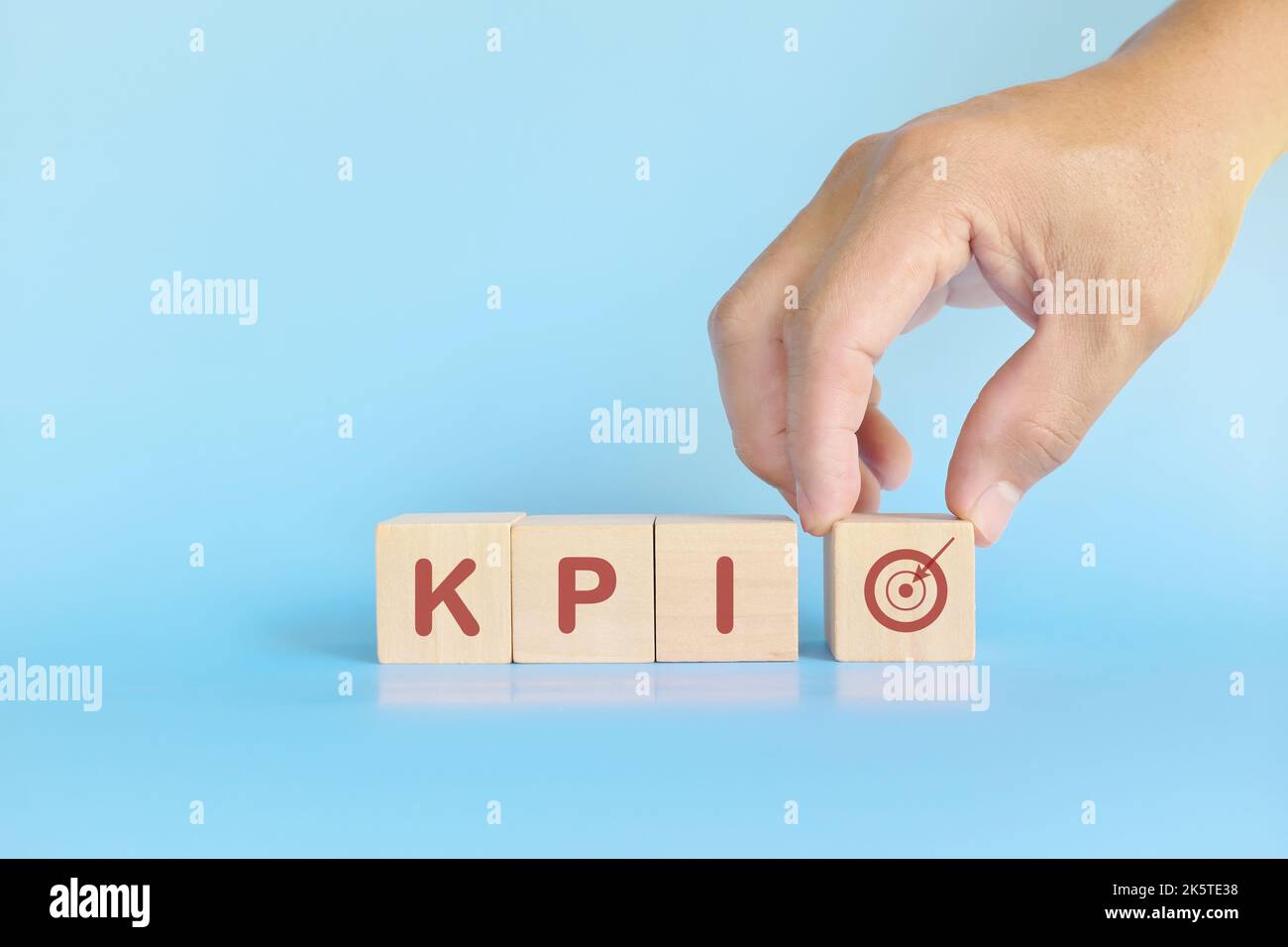 KPI oder Key Performance Indicator Business Target und Establishment Concept. Menschliche Hand stapelt Holzblöcke auf blauem Hintergrund. Stockfoto