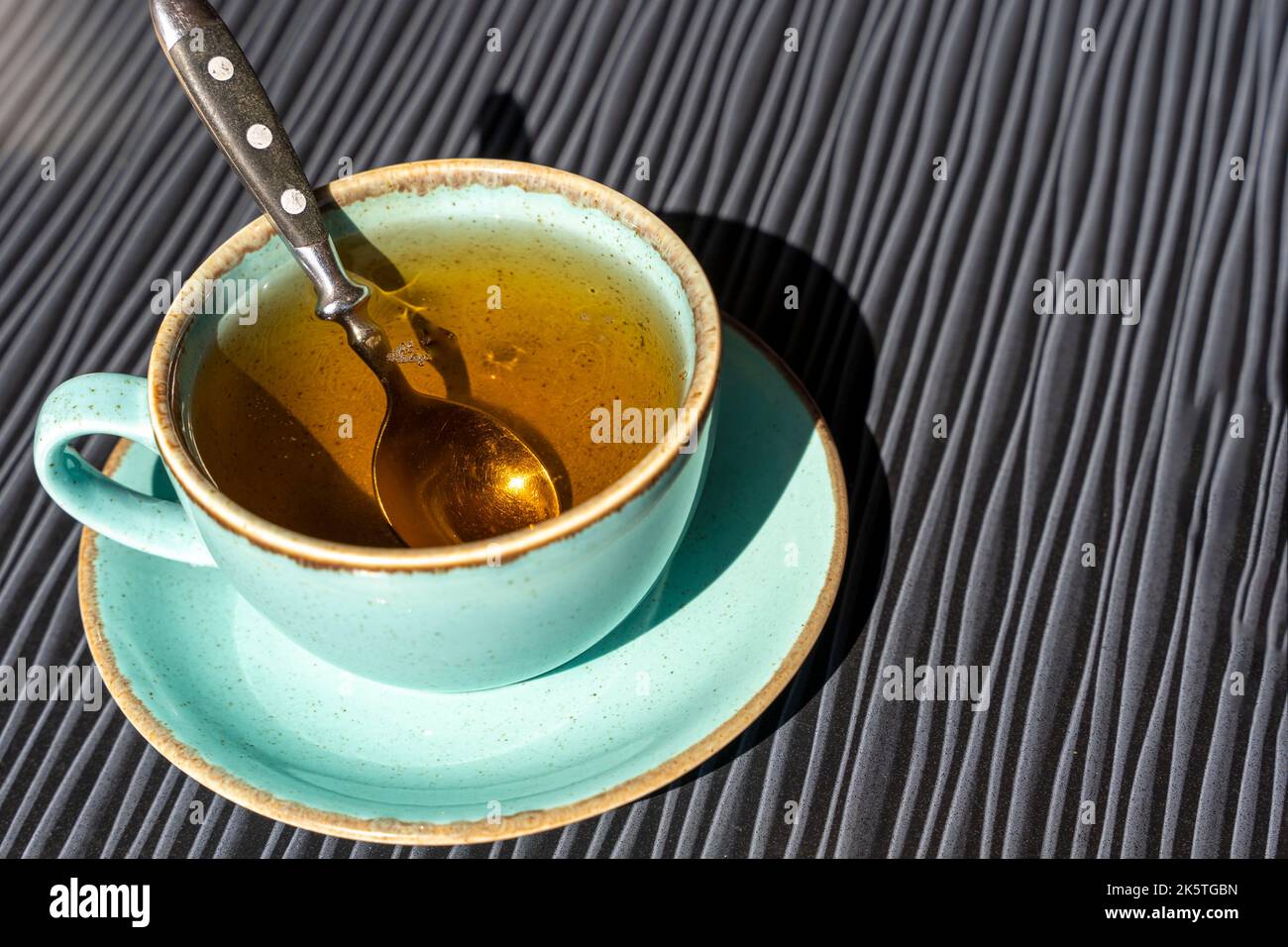 Türkisfarbene Tasse heißen Tee auf einem Tisch im Sonnenlicht während des Frühstücks Stockfoto