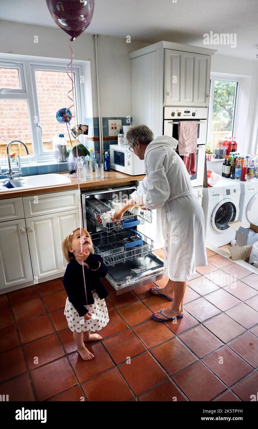 Großmutter bedient die Spülmaschine, während Enkelin einen Ballon fliegt Stockfoto