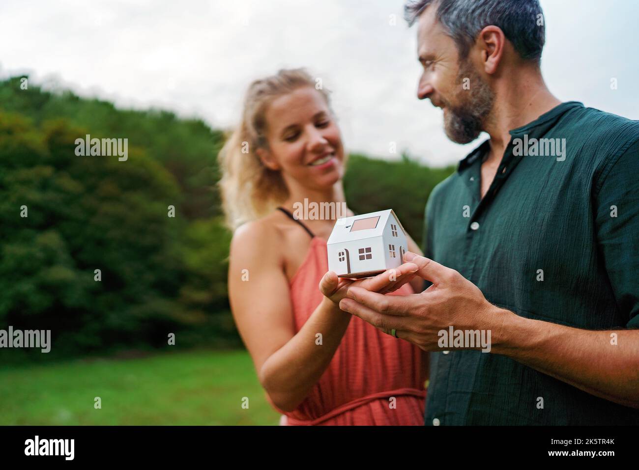 Nahaufnahme eines glücklichen Paares, das ein Papiermodell des Hauses mit Sonnenkollektoren hält und von der Zukunft träumt. Alternative Energie, Ressourcen zu sparen und Stockfoto