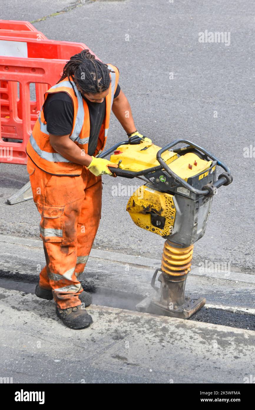 Männliche Arbeiter Nahaufnahme gut sichtbare Kleidung und mechanische whacker vibrierenden Verdichter Werkzeug auf Bürgersteig Straße arbeitet Breitband-Kabel Graben Hinterfüllung UK Stockfoto