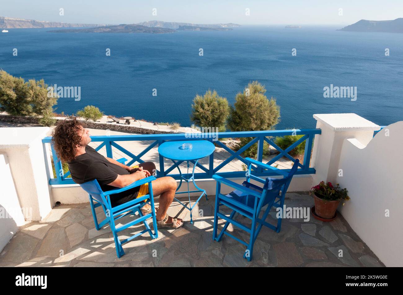 Rückansicht eines Mannes, der auf einem Stuhl auf der Terrasse in Oia sitzt, mit Panoramablick auf die Caldera, die Insel Santorini, Griechenland Stockfoto