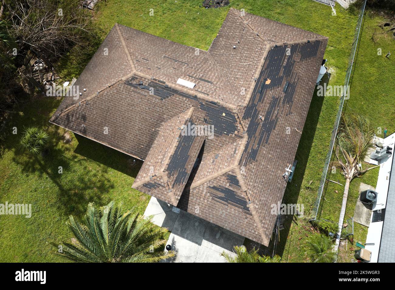 Der Wind beschädigte das Hausdach mit fehlenden Asphaltschindeln nach dem Hurrikan Ian in Florida. Reparatur des Hausdachkonzepts. Stockfoto