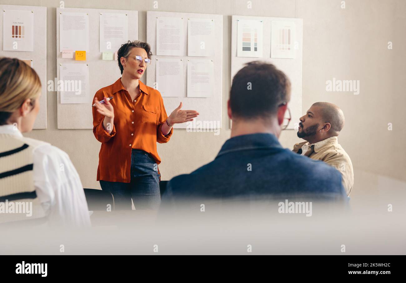 Eine reife Geschäftsfrau, die ihr Team während eines Meetings ihre Idee vor die Hand gibt. Die reife Teamleiterin diskutiert ihre Strategie mit ihren Kollegen. Gruppe von Unternehmen Stockfoto