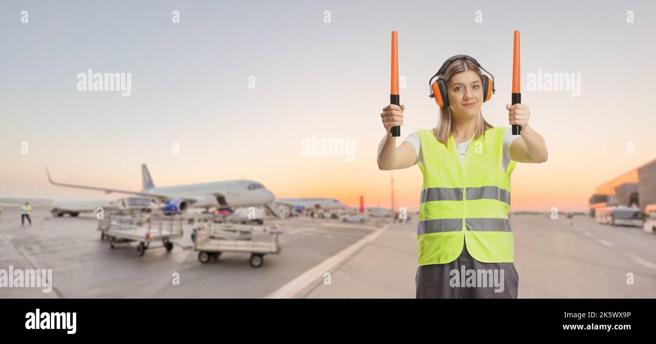 Weibliche Flugzeugmarschall mit Stäben, die auf einem Flughafenvorfeld arbeiten Stockfoto