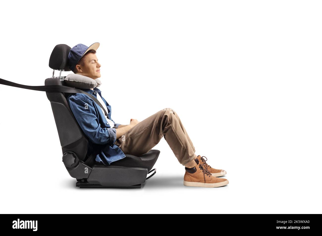 Kerl sitzt in einem Carseat mit einem Sicherheitsgurt und Kissen für seinen Hals isoliert auf weißem Hintergrund Stockfoto