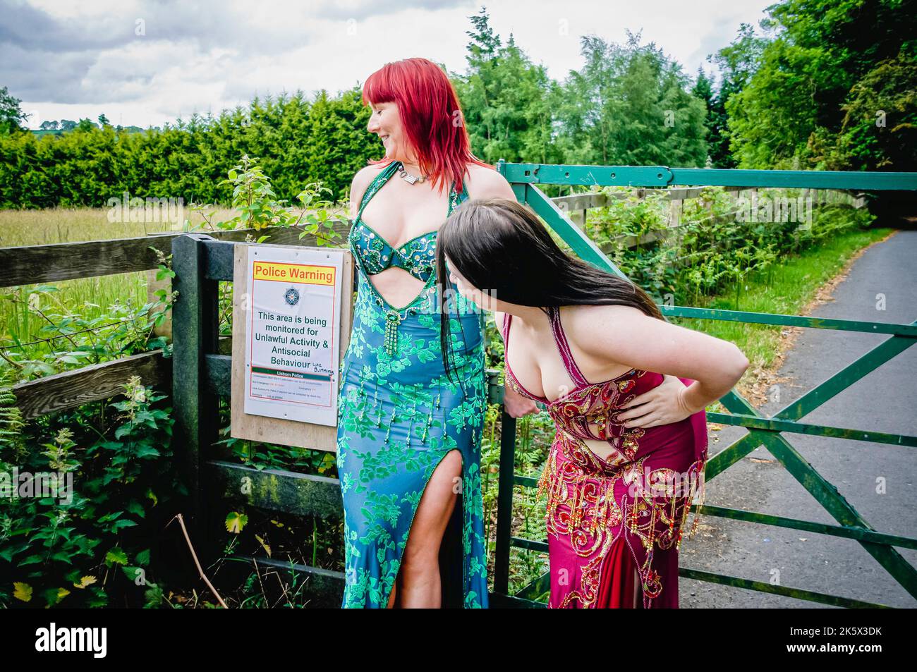 Zwei Bauchtänzerinnen, die ein Kostümkostüm tragen, untersuchen ein Warnschild vor antisozialen Aktivitäten in einem ländlichen Gebiet. Stockfoto