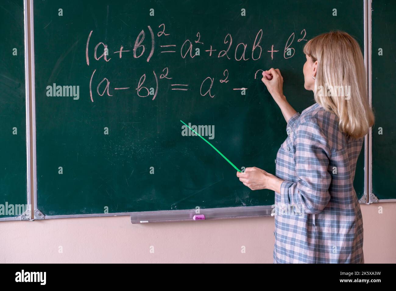 Eine junge kaukasische Mathematiklehrerin steht an der Tafel und erklärt die Lösung eines mathematischen Problems Stockfoto