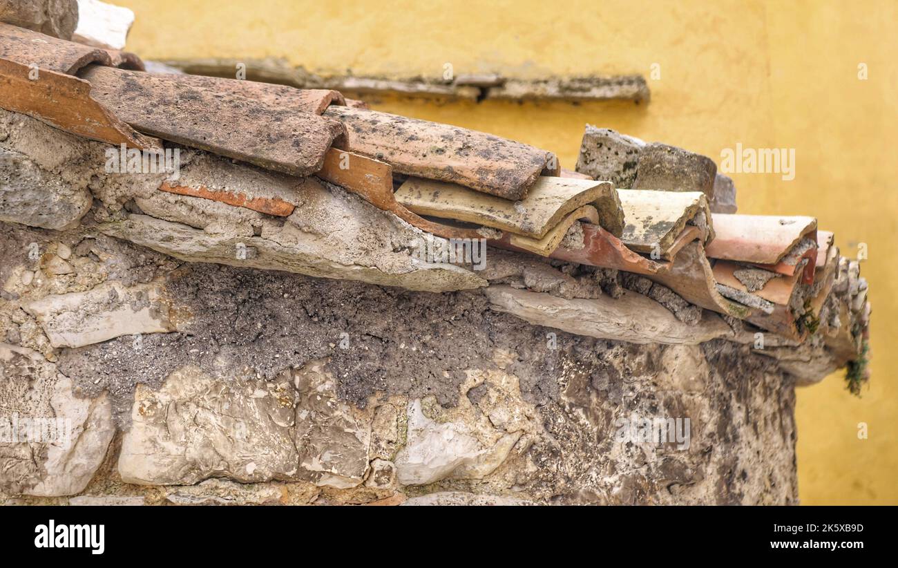 Alte Dachziegel, verfaulte und zerstörte Dachziegel auf einem Steinhaus Stockfoto