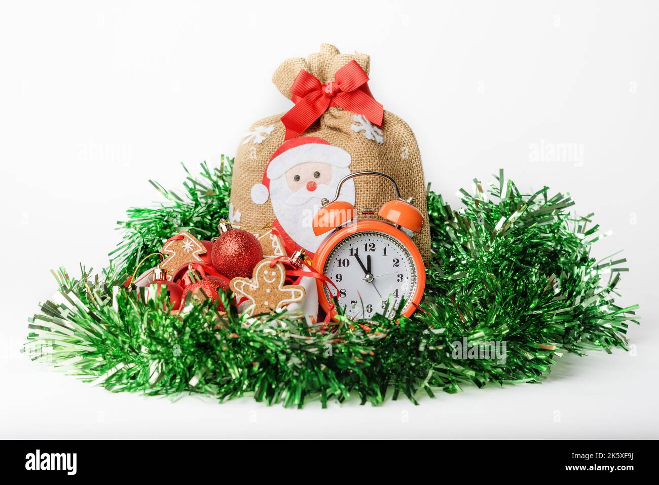 Konzeptfoto eines Silvesterabends, Wecker, eine Tasche mit Geschenken und Weihnachtsbaumschmuck in einem Weihnachtsmannhut, isoliert auf einem weißen Hintergro Stockfoto