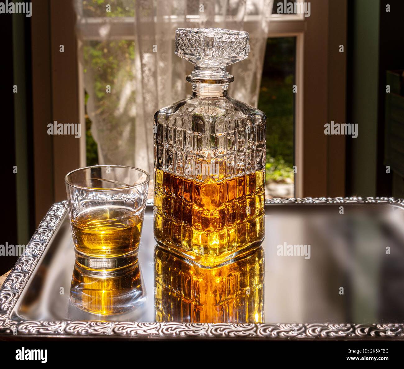 Whiskey in dekorierter Kristallglasflasche, Whiskey oder Bourbon in Vintage-Flasche mit Glas auf silbernem Tablett, das im Zimmer mit Hintergrundbeleuchtung dekoriert ist Stockfoto