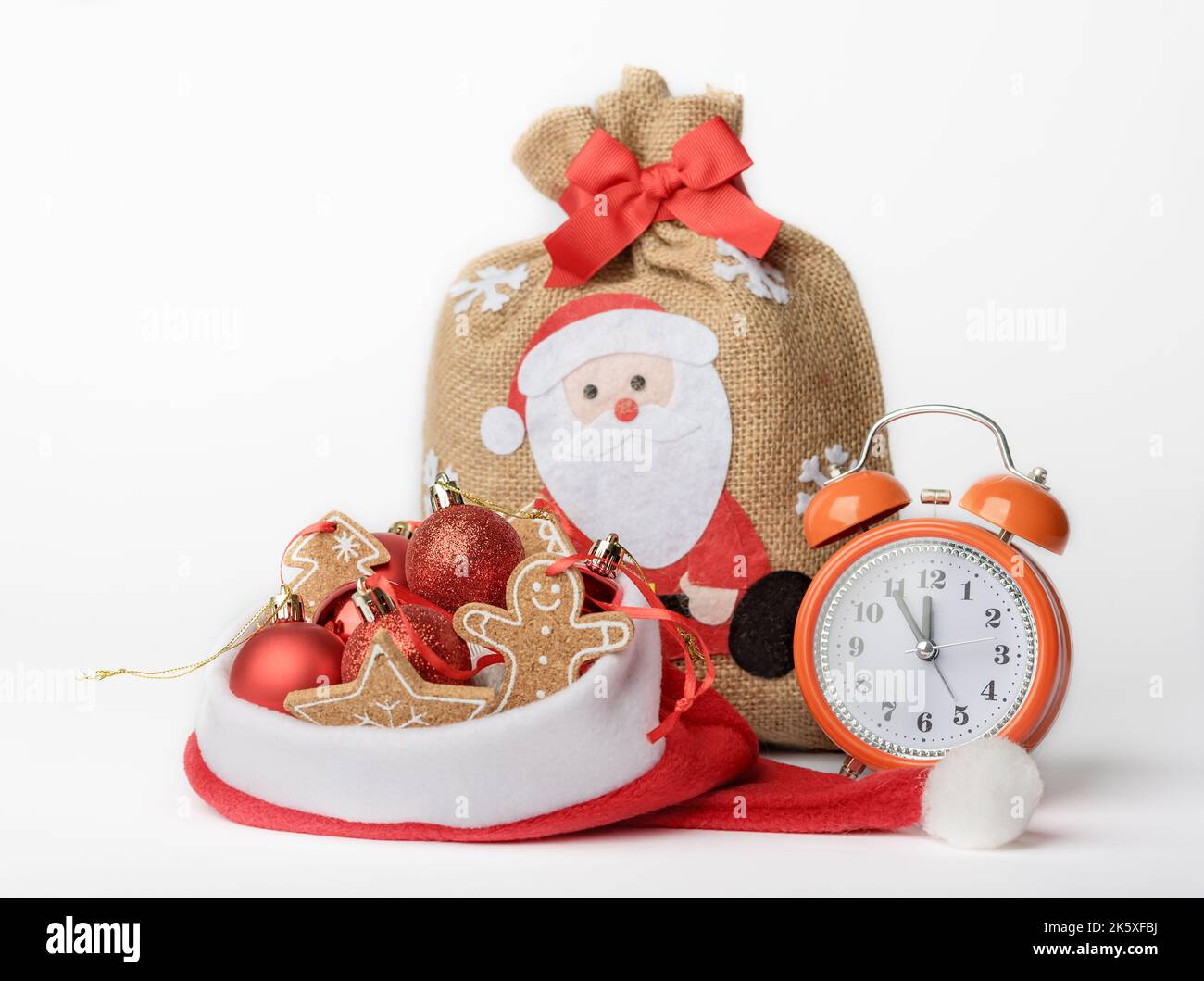 Konzeptfoto eines Silvesterabends, Wecker, eine Tasche mit Geschenken und Weihnachtsbaumschmuck in einem Weihnachtsmannhut, isoliert auf einem weißen Hintergro Stockfoto