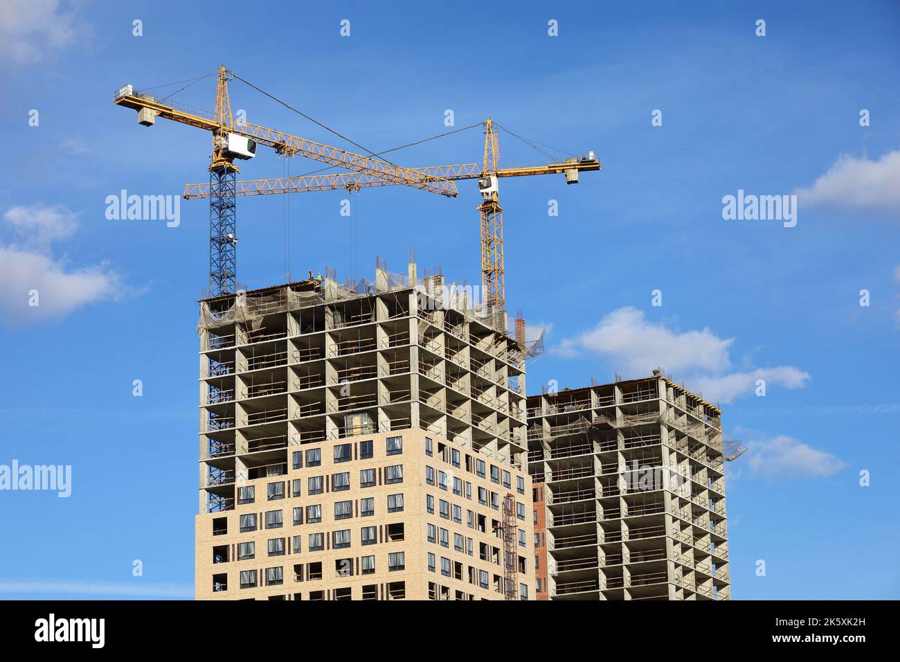 Turmkräne und unfertige Gebäude auf dem Hintergrund des blauen Himmels mit weißen Wolken. Wohnungsbau, Wohnblocks in der Stadt Stockfoto
