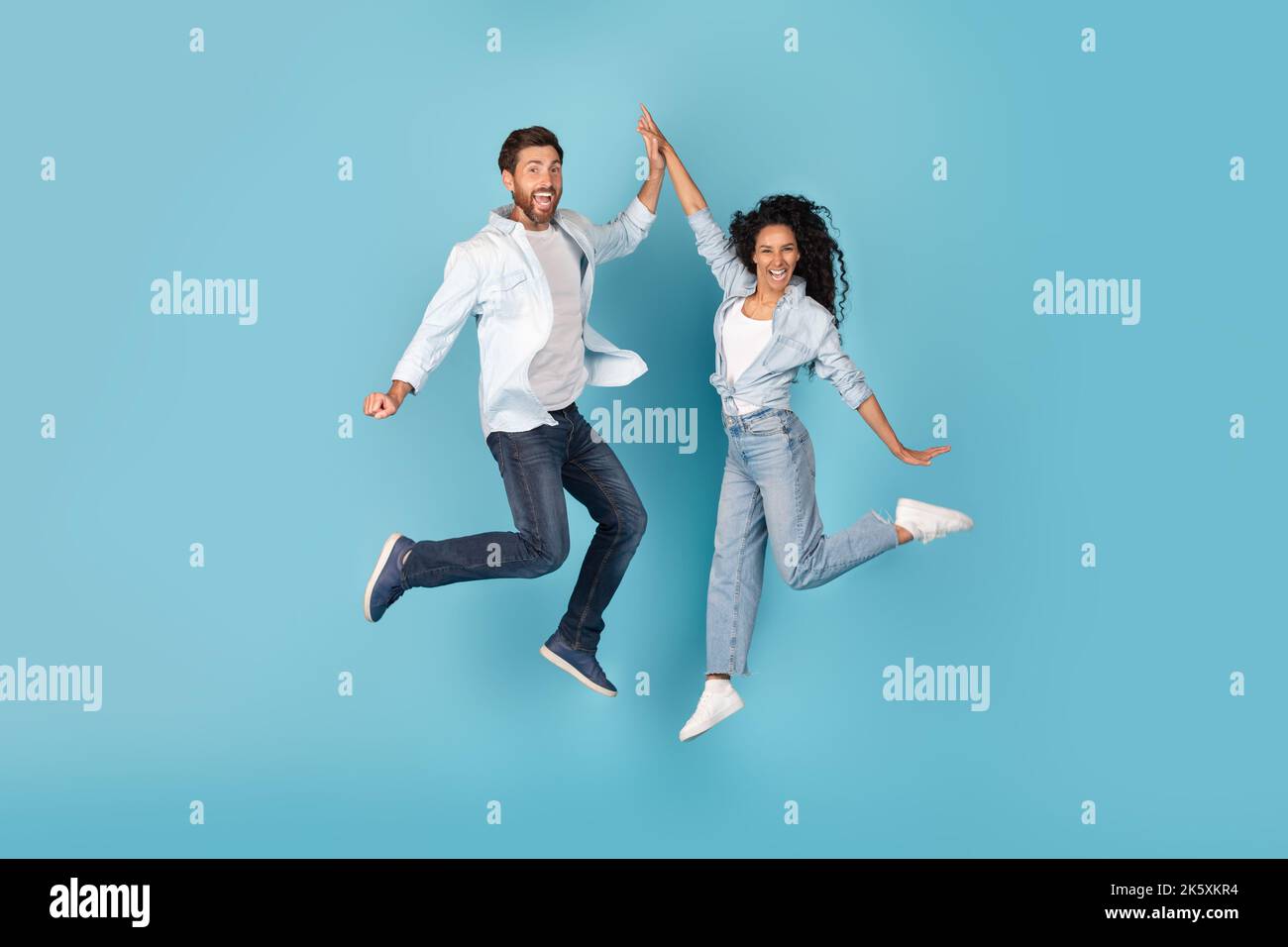 Aufgeregt fröhlich tausendjährigen kaukasischen und arabischen Paar in der Luft springen, geben hohe fünf, auf freien Raum Stockfoto