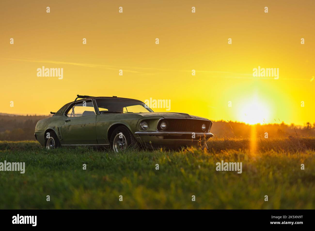 Old american Muscle Car in grüner Farbe, Foto in flachem Profil und am Abend Sonnenuntergang mit Sonne nahe am Horizont aufgenommen. Romantisches Oldtimer Auto Foto. Stockfoto