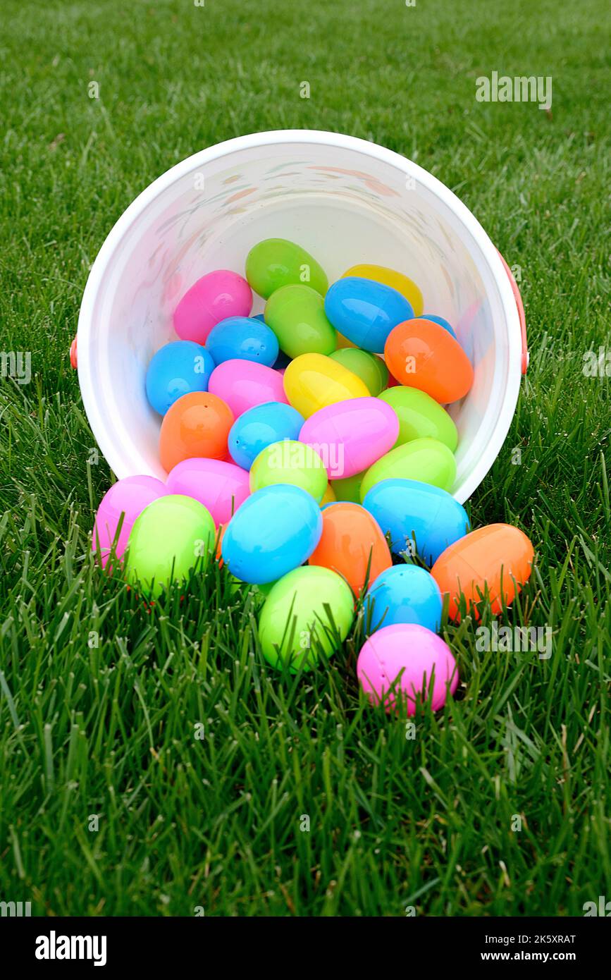 Bunte Plastiköstereier, die aus dem Eimer auf grünes Gras auslaufen Stockfoto