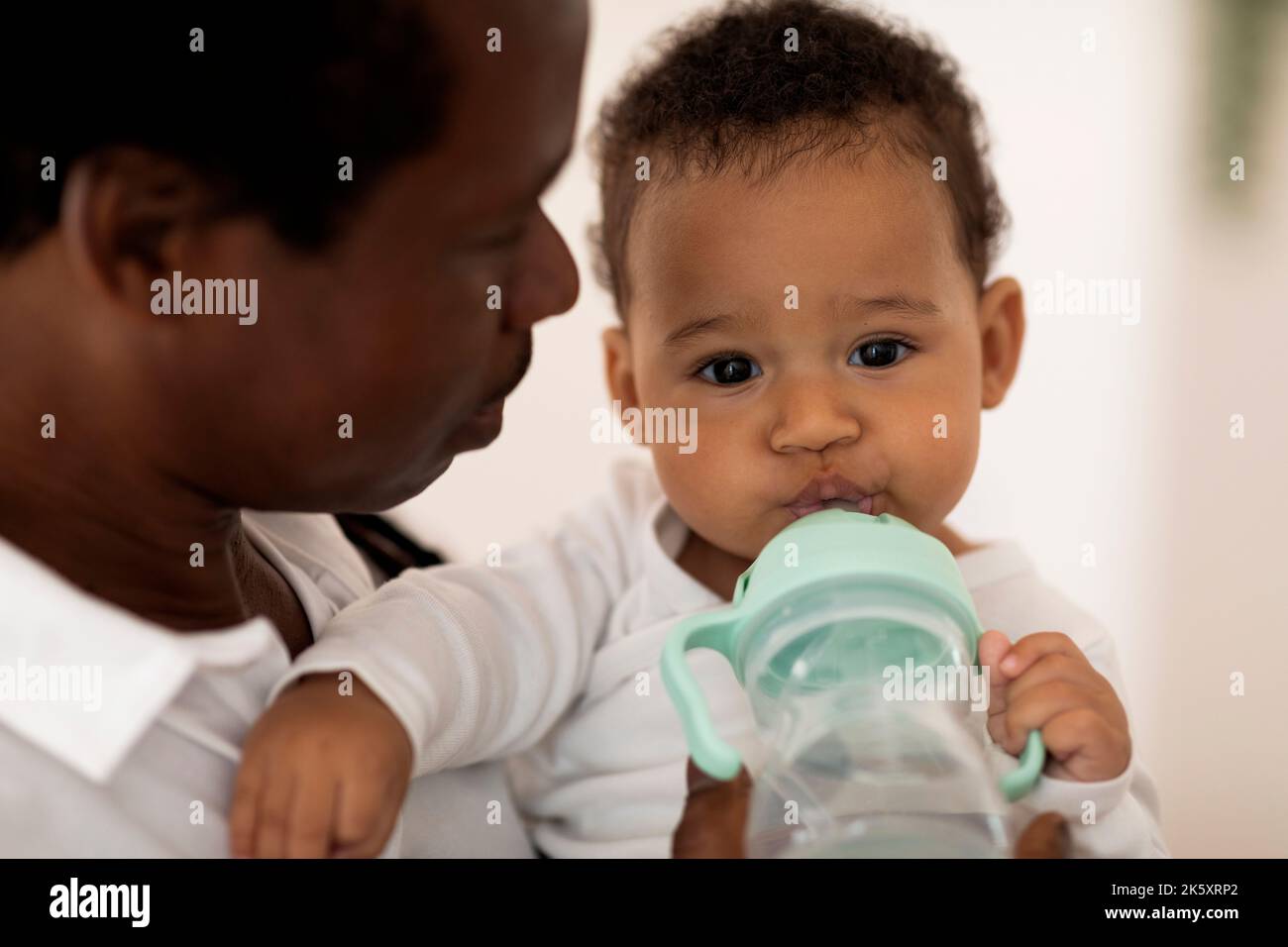 Entzückendes schwarzes Baby Trinkwasser aus Flasche beim Entspannen in den Händen des Vaters Stockfoto