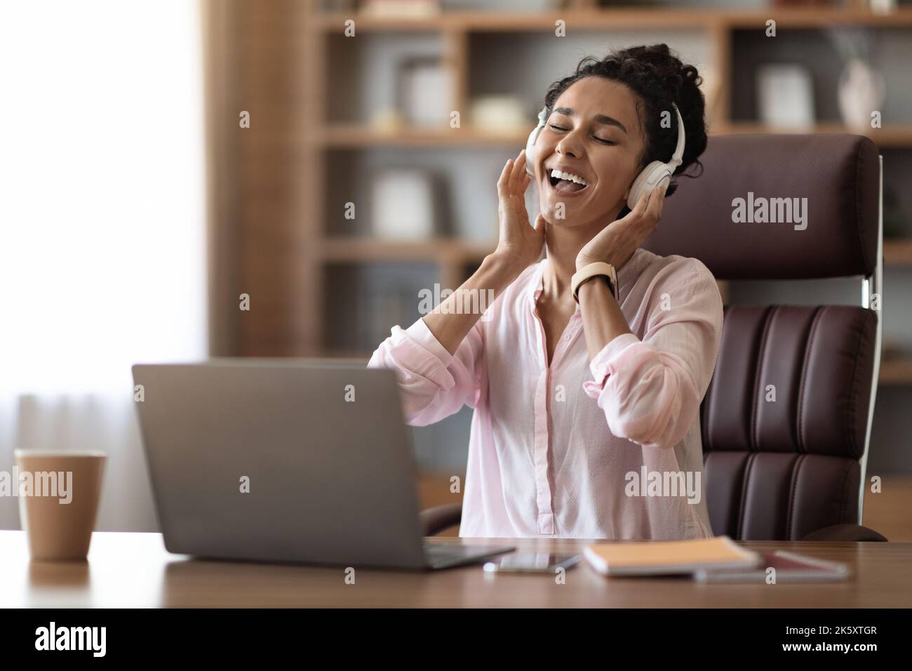 Glückliche junge Geschäftsfrau, die im Büro Musik hört und singt Stockfoto