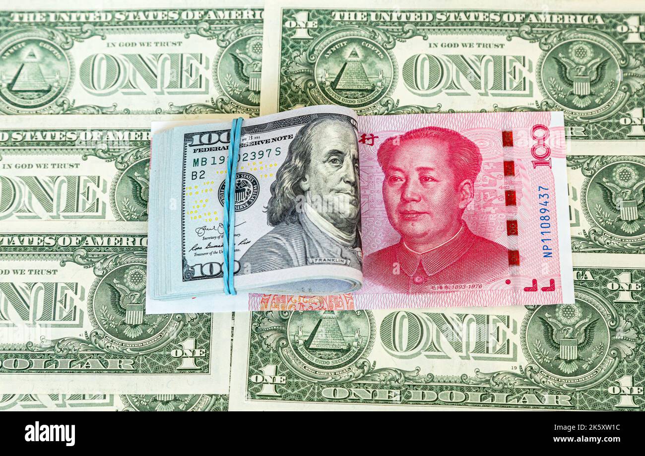 Gefaltete amerikanische Dollar-Banknoten, umwickelt von Gummiband und chinesischer Banknote mit Mao-Zedong-Porträt. Selektiver Fokus Stockfoto