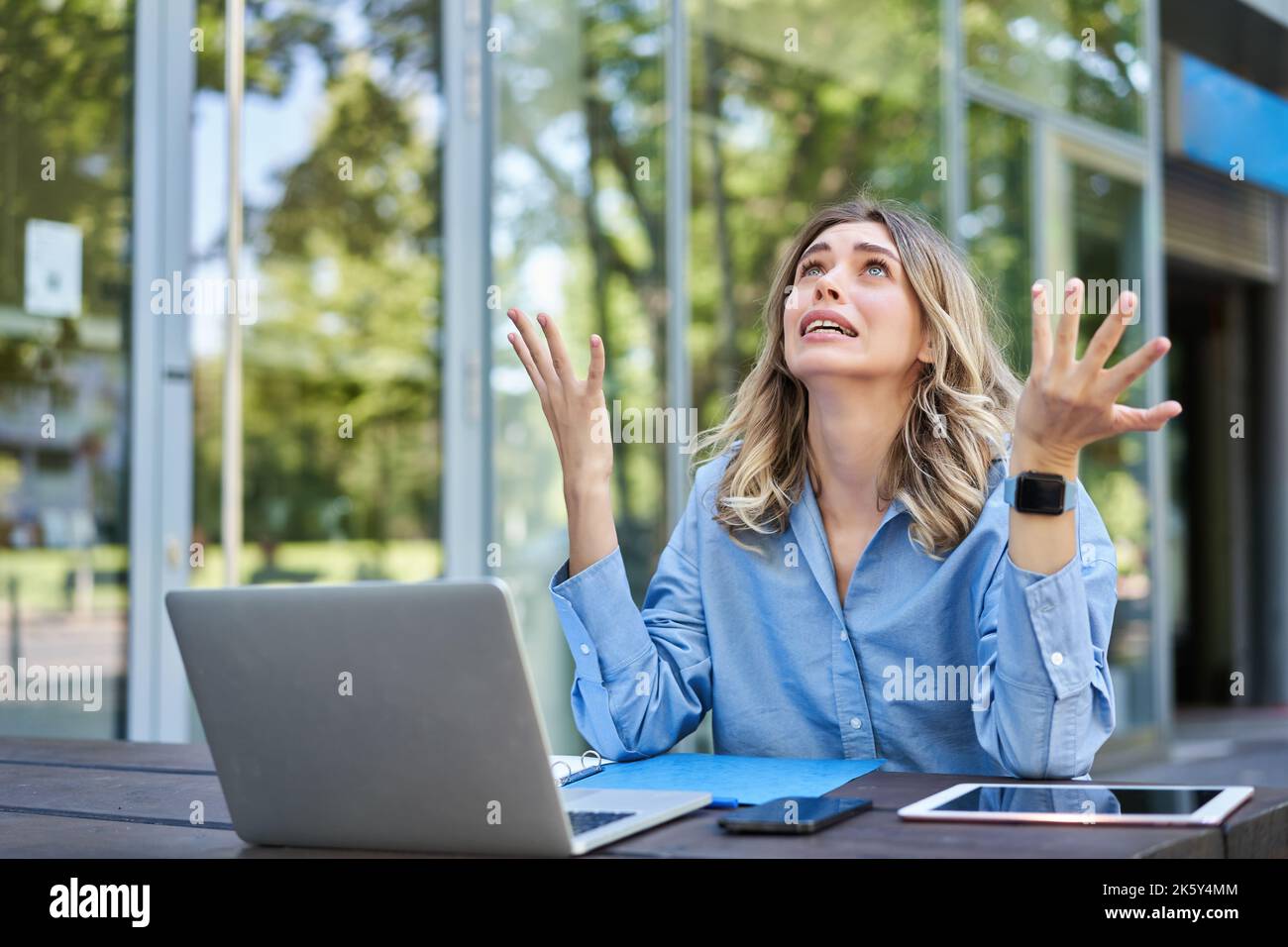 Enttäuschte junge Geschäftsfrau, die sich frustriert fühlte, mit einem Laptop draußen auf der Straße saß, aufschaute und sich beschwerte Stockfoto