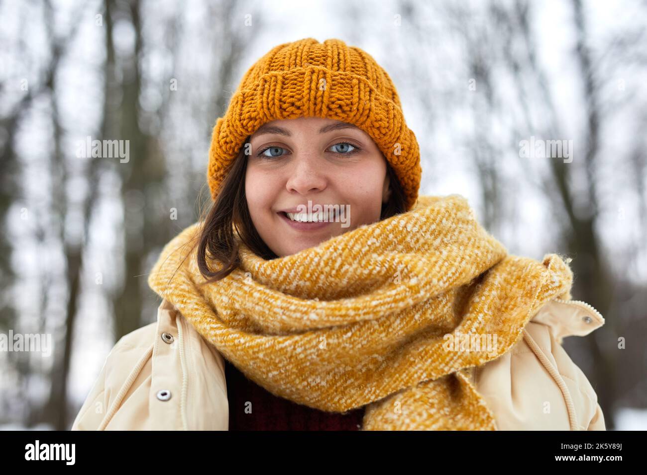 Vorderansicht Porträt der kaukasischen jungen Frau trägt Strickmütze und Schal im Winterwald und lächelt an der Kamera Stockfoto