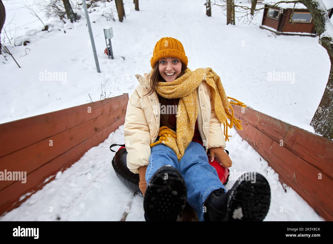 Hochwinkelsportrait einer aufgeregt jungen Frau, die im Winter bergab Schlitten fährt und Spaß an Outdoor-Aktivitäten genießt Stockfoto