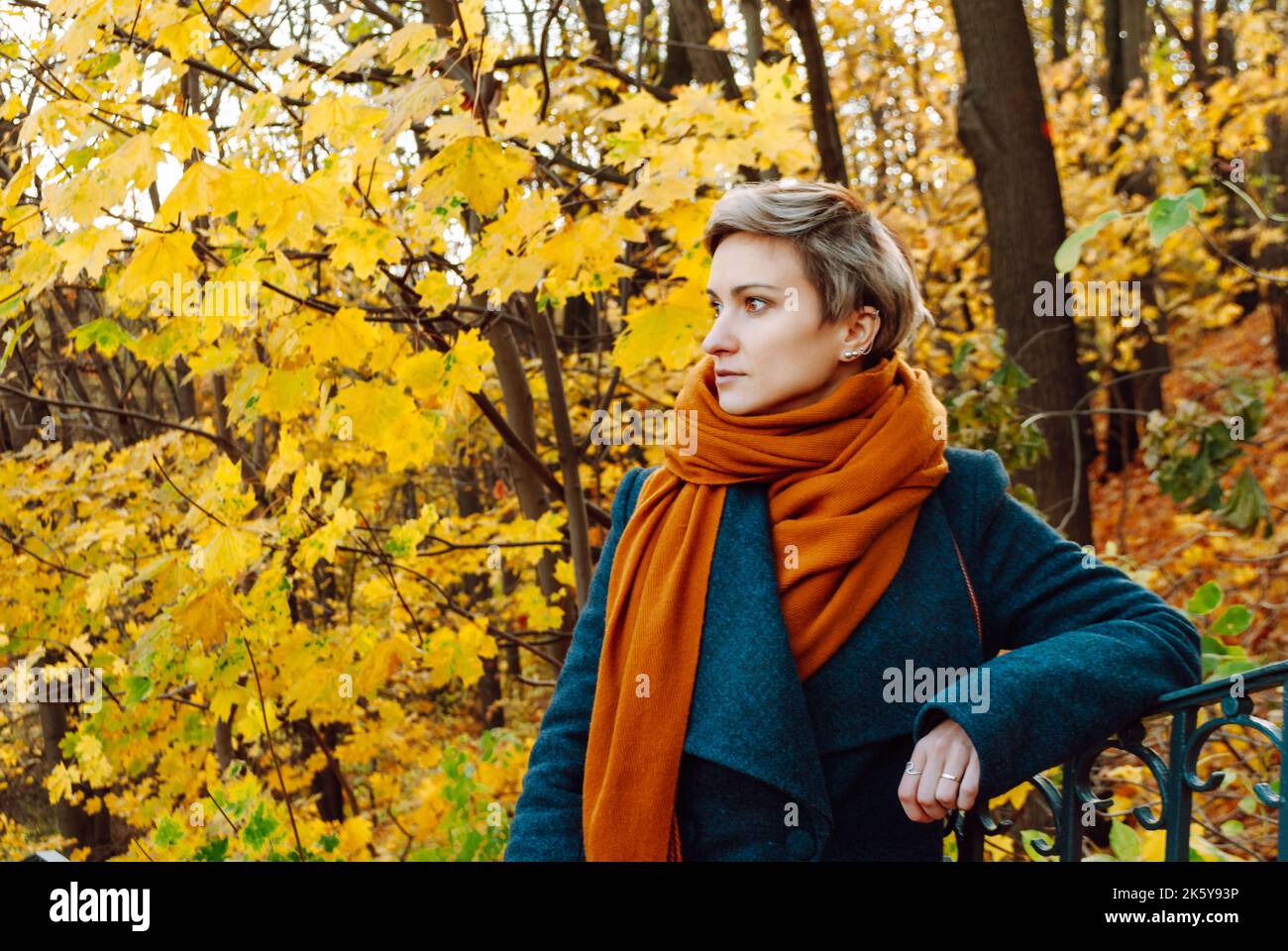 Kurzhaarige Frau gegen herbstliche Ahorne im Mantel und einem orangefarbenen Schal Stockfoto