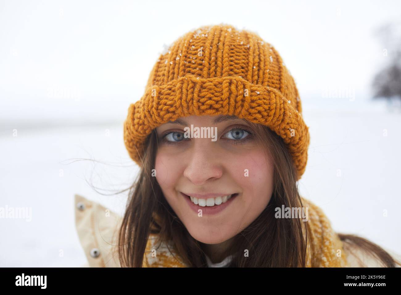 Aufsehendes Porträt einer jungen Frau im Winter, lächelnd auf die Kamera mit leuchtend blauen Augen, Kopierraum Stockfoto