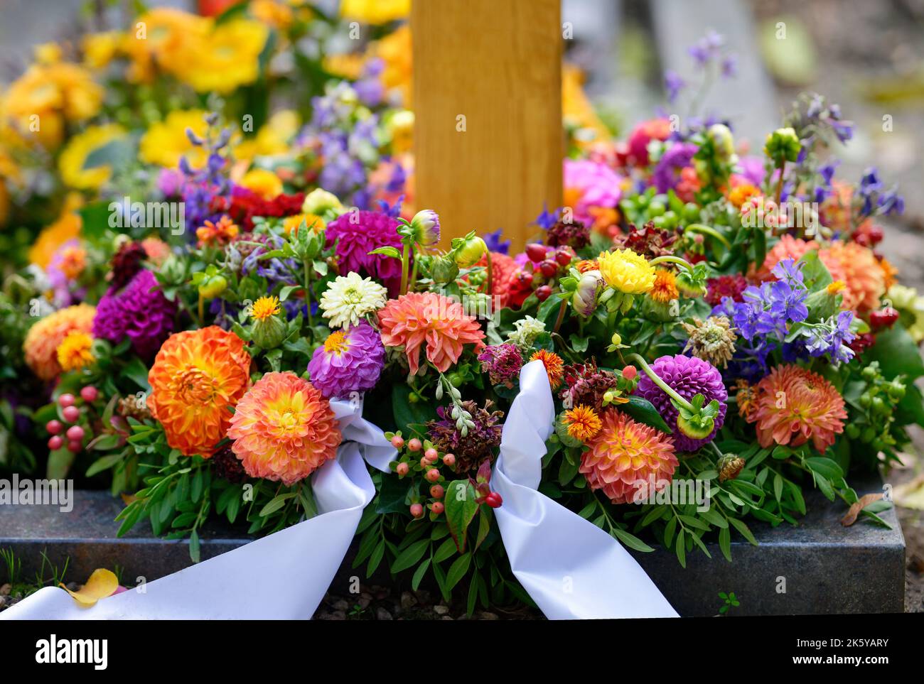 Trauerkranz mit weißen Bändern und bunten Blumen auf einem Grab Stockfoto