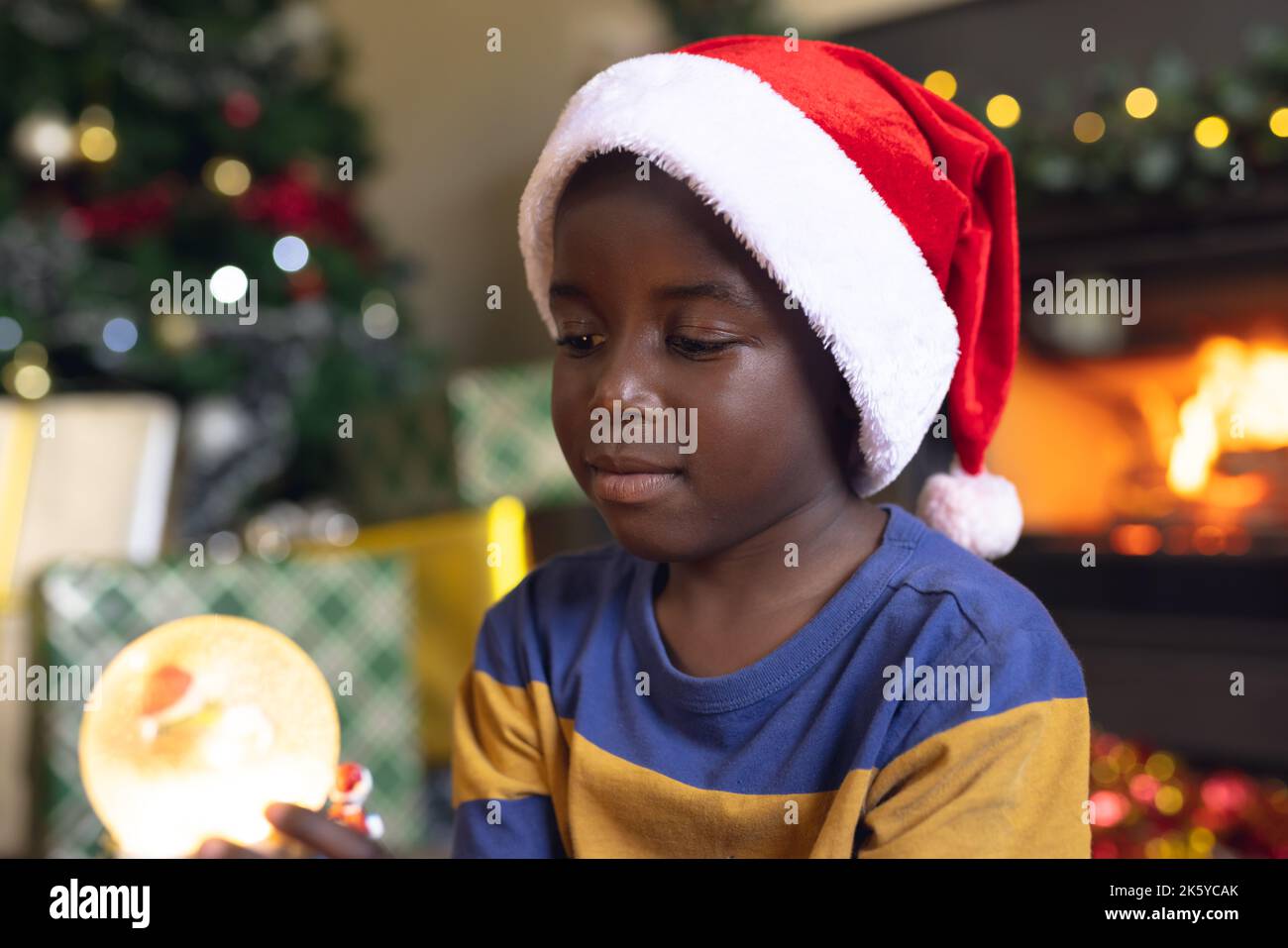 Ein glücklicher afroamerikanischer Junge, der einen weihnachtsschneeball hält und am nächsten Kamin sitzt Stockfoto