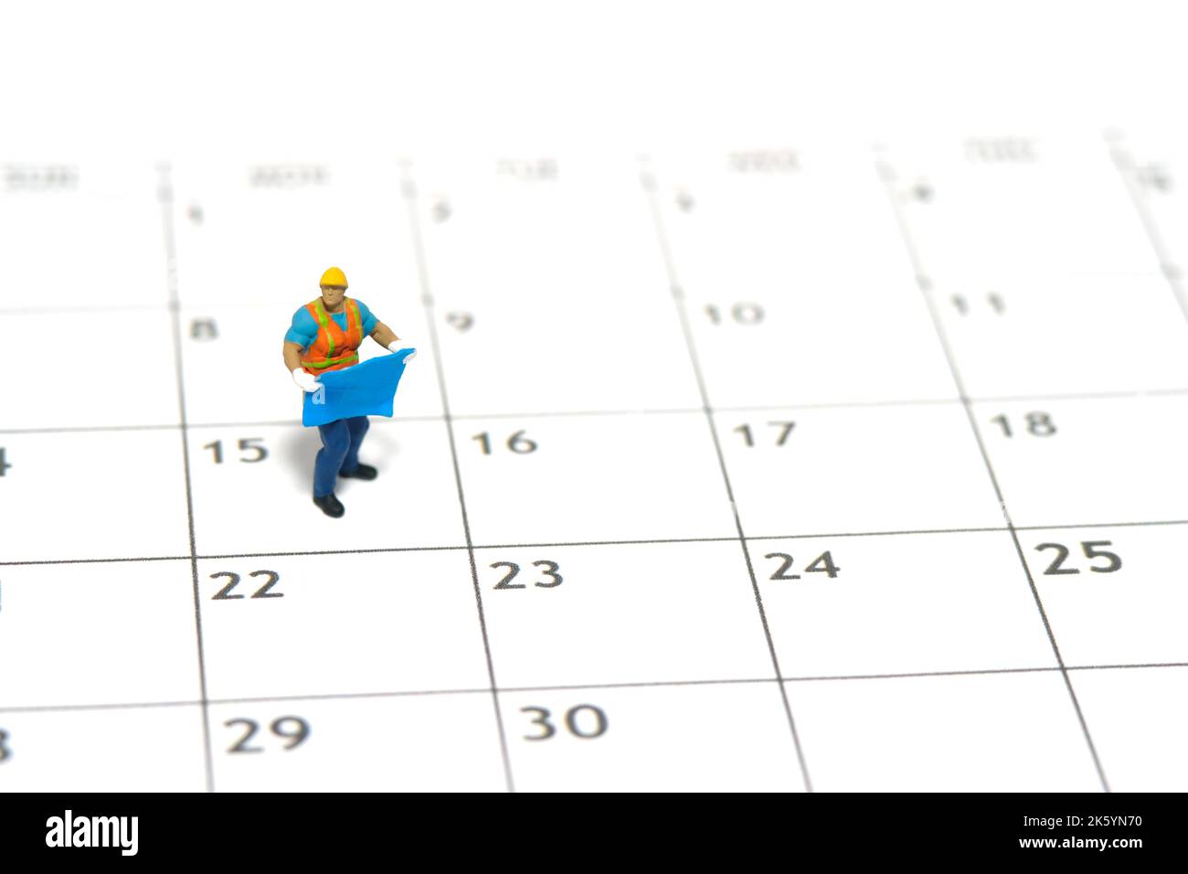 Miniatur Menschen Spielzeug Figur Fotografie. Zeitmanagement-Konzept für Projekttermine. Ein Bauarbeiter mit Blaupause, der über dem Kalender steht. Ist Stockfoto