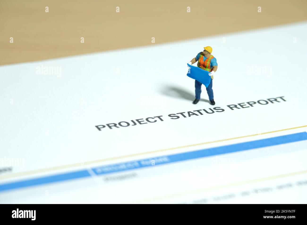 Miniatur Menschen Spielzeug Figur Fotografie. Projektstatusbericht Konzept. Ein Bauarbeiter, der eine Blaupause über der Fortschrittsbericht-Datei hält Stockfoto