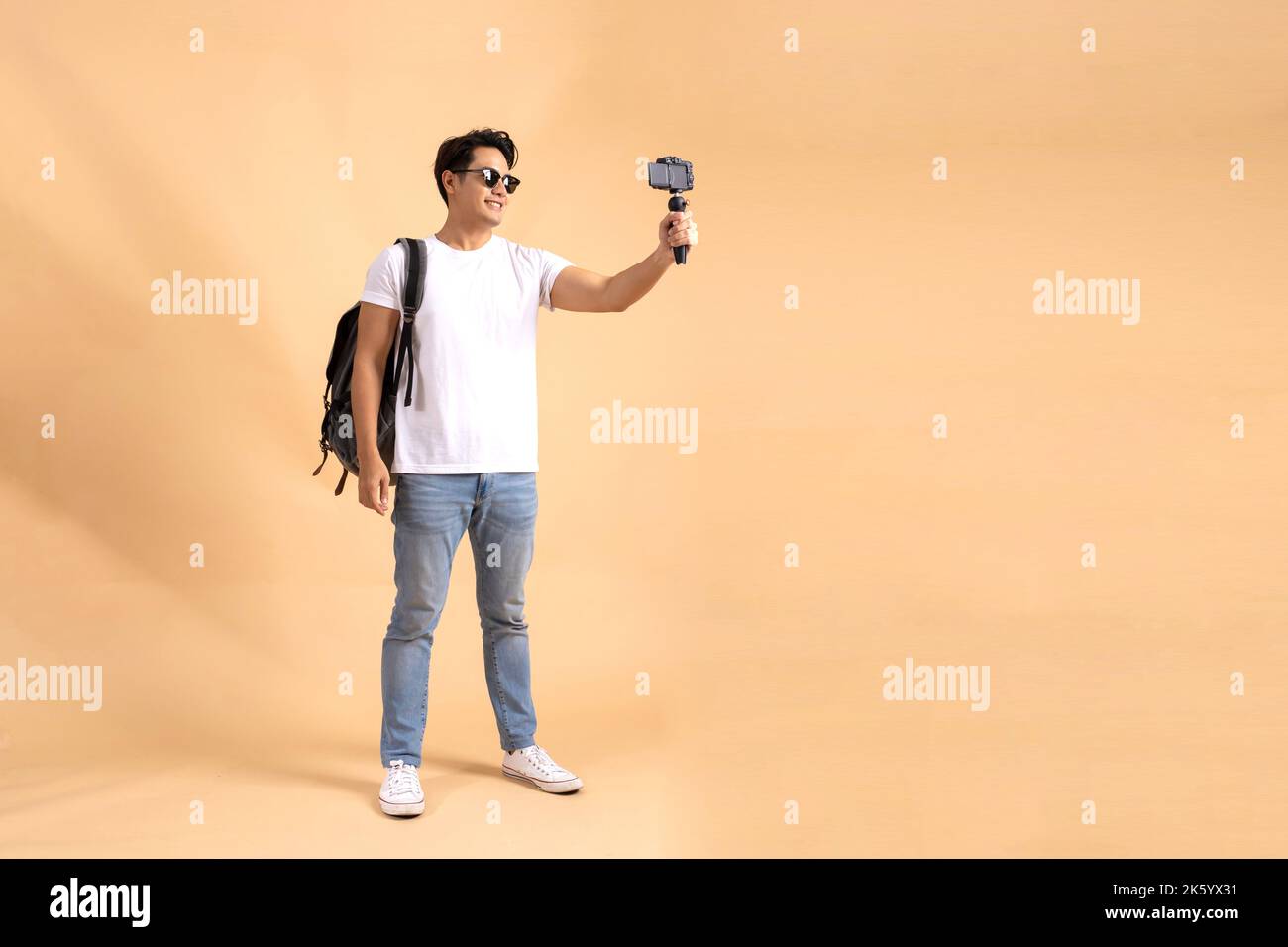 Junger asiatischer Tourist Backpacker Mann lächelt und nimmt ein Selfie und Blog isoliert auf beigem Hintergrund Stockfoto