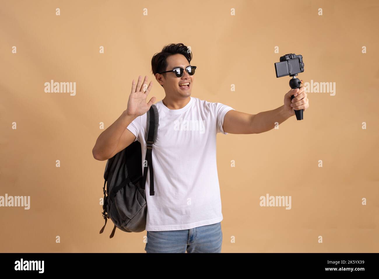 Junger asiatischer Tourist Backpacker Mann lächelt und nimmt ein Selfie und Blog isoliert auf beigem Hintergrund Stockfoto