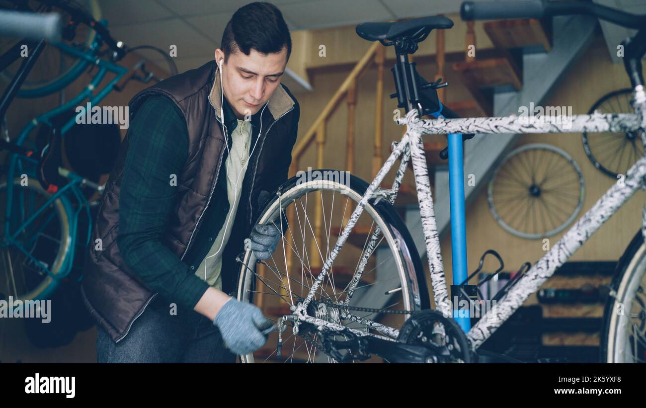 Erfahrener Mechaniker in Handschuhen montiert das Hinterrad des Fahrrads während der Wartung des Fahrzeugs am Arbeitsplatz. Professionelle Instrumente, Ersatzteile und Geräte sind sichtbar. Stockfoto