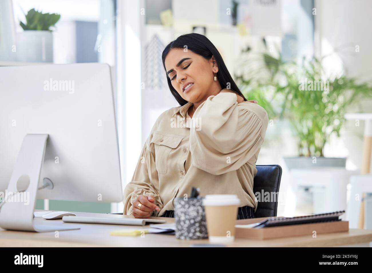Eine Geschäftsfrau mit gemischter Rasse, die unter Nackenschmerzen leidet, während sie sich massiert und versucht, Schmerzen und Anspannung bei einem Bürojob zu lösen. Jung Stockfoto
