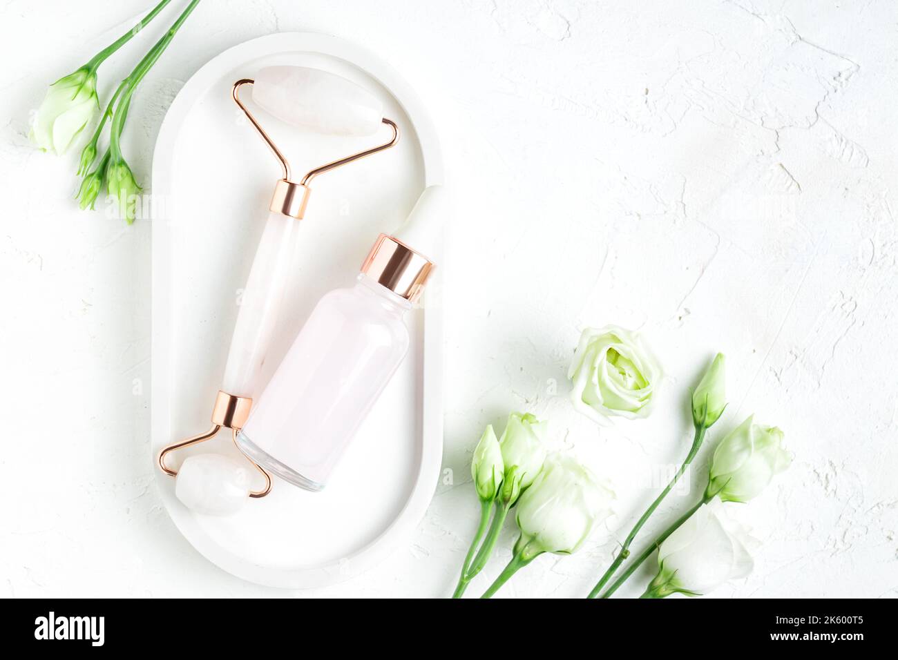 Schöne Komposition aus nicht gebrandeter Serumflasche, rosa Quarzstein Gesichtswalze auf weißem Hintergrund. Anti-Aging-Kosmetik-Konzept. Kreative trendige Cos Stockfoto