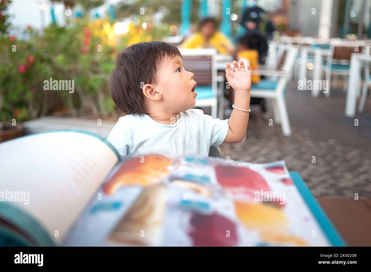 Ein gutaussehender, gemischter Junge, der einen Jahr alt war und den Kellner anrief, um sein Essen in einem nicht erkennbaren Restaurant zu bestellen und zu wählen Stockfoto